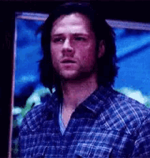 a man in a blue plaid shirt is standing in front of a blue background .
