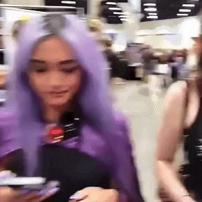 a woman with purple hair is holding a cell phone in her hand