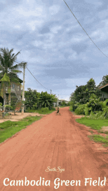 a person riding a bike down a dirt road that says cambodia green field