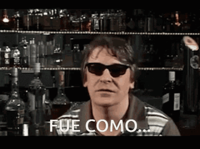 a man wearing sunglasses says fue como in front of a bar full of bottles