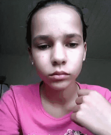 a young girl in a pink shirt is making a funny face with her hand .