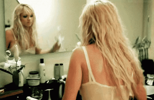 a woman is standing in front of a bathroom mirror looking at herself .