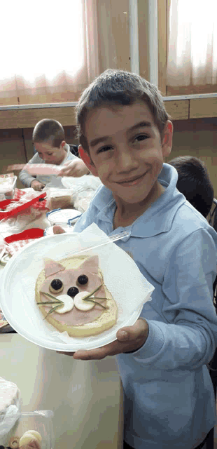 a young boy holds up a plate of food with a cat sandwich on it