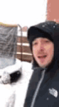 a man in a black jacket and hat is standing in the snow .