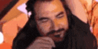 a man with a beard is wearing headphones and looking at the camera with his eyes closed .