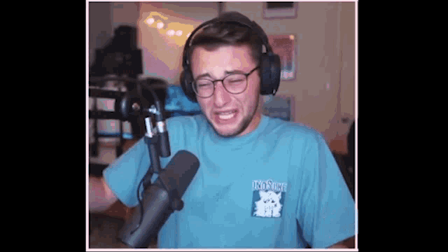 a man wearing headphones and a blue shirt is standing in front of a microphone .