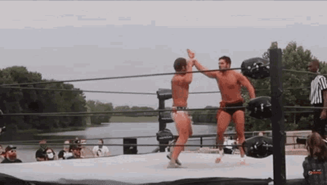 two men are wrestling in a ring with a referee in the background