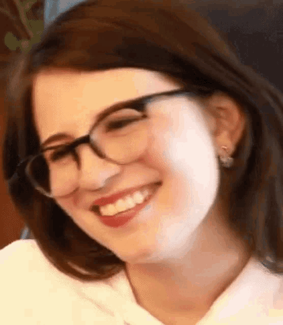 a woman wearing glasses and earrings is smiling and looking at the camera .