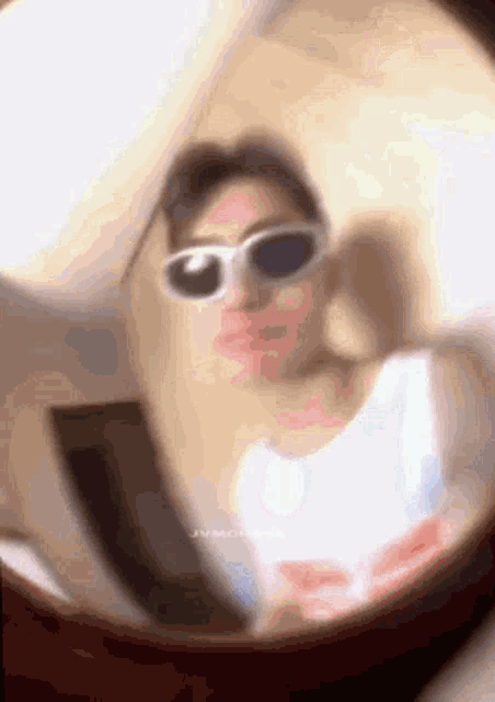 a blurry picture of a person wearing sunglasses and taking a selfie in a mirror .