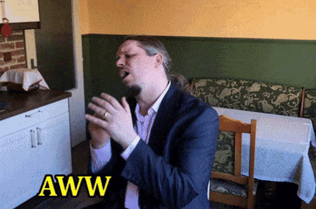 a man in a suit is sitting at a table with the word aww written above him