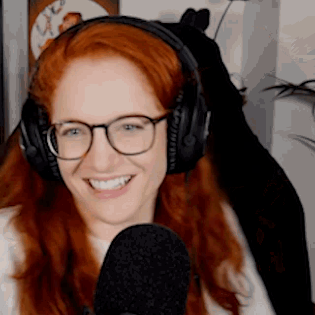 a woman with red hair and glasses is wearing headphones and smiling into a microphone .