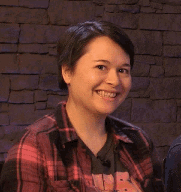 a woman wearing a plaid shirt is smiling and giving a thumbs up