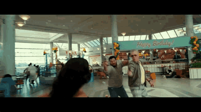 two men are dancing in front of a sign that says " happy birthday "