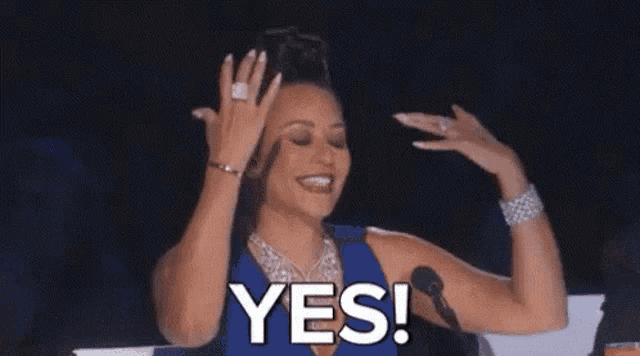 a woman is sitting in front of a microphone with her hands in the air and saying yes .