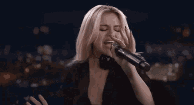 a woman is singing into a microphone while wearing a black jacket .