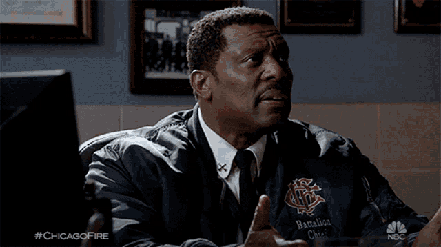 a man in a battalion chief jacket is sitting at a desk