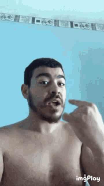 a shirtless man with a beard is making a funny face with his finger