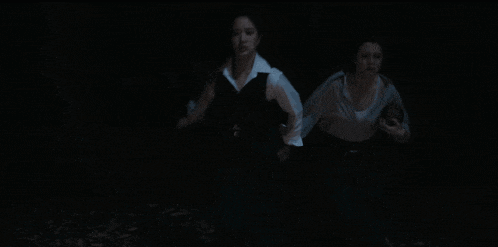 a couple standing in a dark room with leaves on the floor