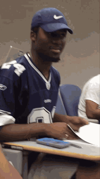 a man wearing a blue hat and a dallas jersey sits at a desk