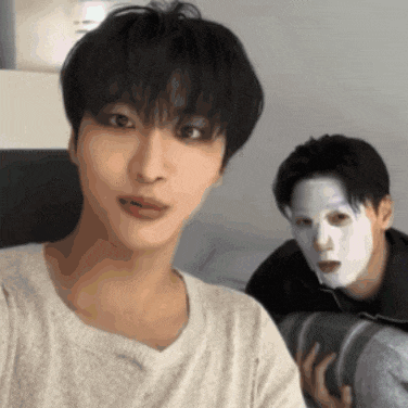 a man with a white mask on his face looks at the camera while another man looks on .
