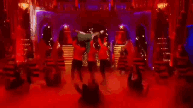 a group of people are dancing in a dark room with lightsabers in their hands