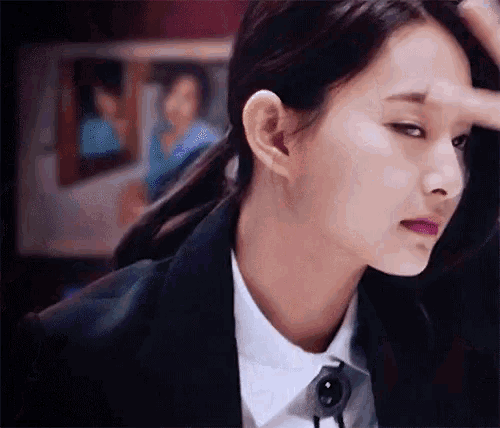 a woman in a suit and white shirt is touching her forehead with her hand .
