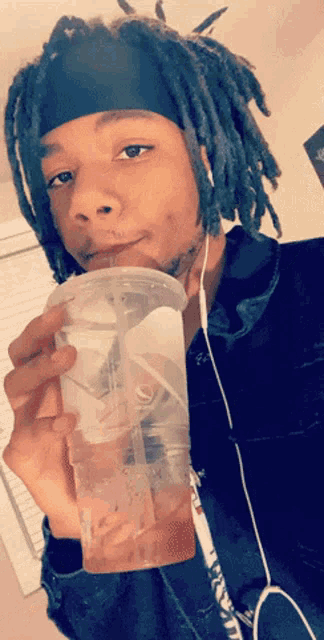 a man with dreadlocks is holding a plastic cup with a straw