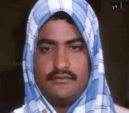 a man with a mustache and a scarf around his head is making a funny face .