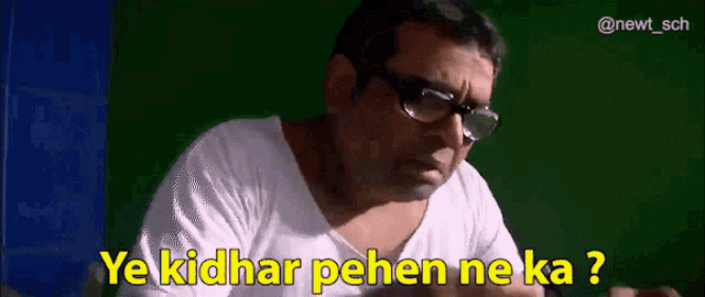 a man wearing glasses and a white shirt is sitting in front of a green screen and says ye kidhar pehen ne ka ?