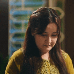 a woman with long brown hair is wearing a yellow shirt and making a funny face .