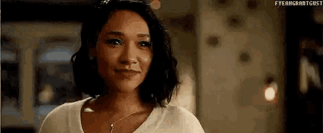 a woman is smiling and looking at the camera while wearing a white sweater and a necklace .