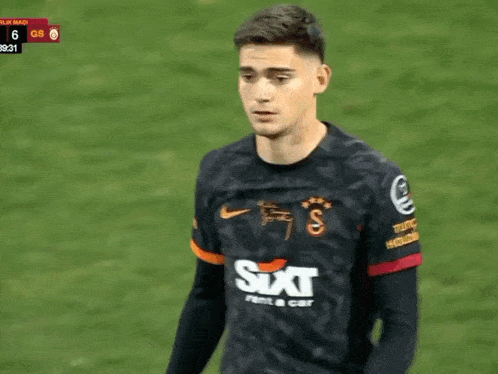a soccer player wearing a sixt shirt stands on a field .