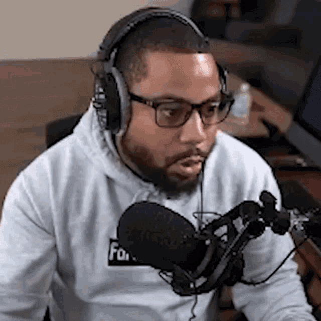 a man wearing headphones and glasses is sitting in front of a microphone and talking into it .