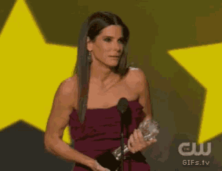 a woman in a purple dress is holding a trophy and speaking into a microphone .