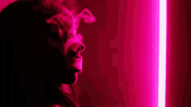 a woman is smoking a cigarette in a dark room in front of a pink neon light .