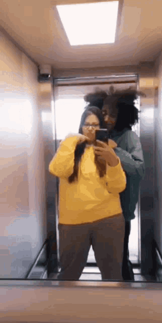 a woman in a yellow sweater is taking a selfie with a man in an elevator .