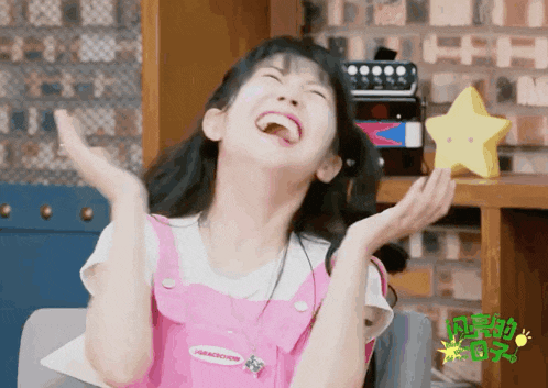 a girl wearing pink overalls and a shirt that says parachute laughs with her hands in the air
