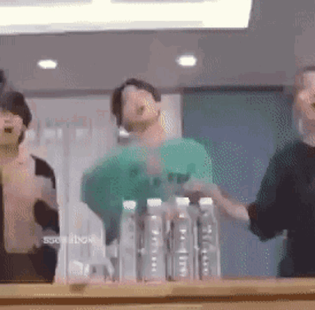 a group of people are dancing in front of a mirror in a room with bottles of water .