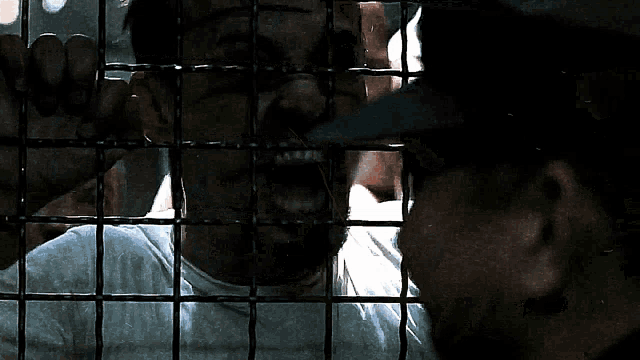 a man behind a fence talking to another man behind it