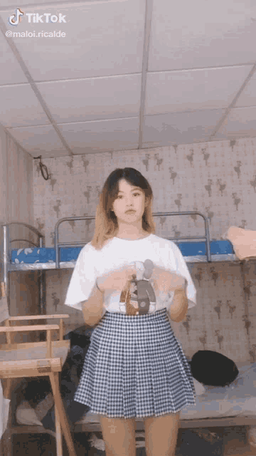 a girl in a plaid skirt and a white shirt with a teddy bear on it stands in front of bunk beds