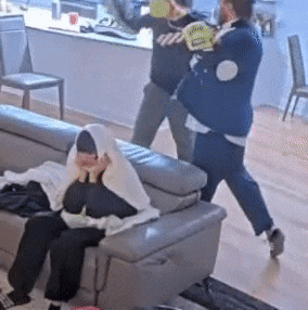 a man is standing next to a woman sitting on a couch while another man throws a frisbee .