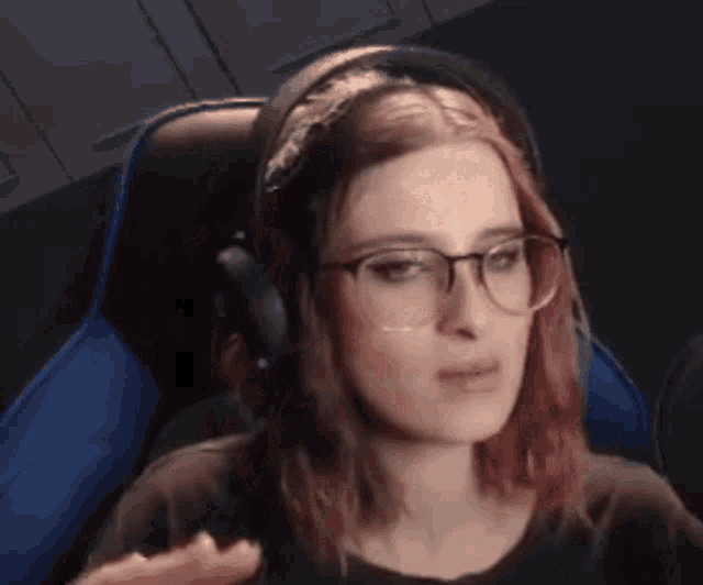a woman wearing glasses and headphones is sitting in a chair and making a funny face .