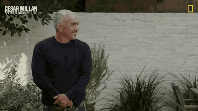 a man stands in front of a brick wall with the words cesar millan better humans better dogs on the bottom