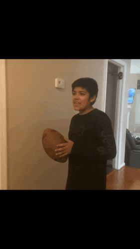 a young boy in a black shirt is holding a football and smiling