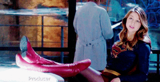 a woman in a superhero costume is sitting on a table with her feet up and smiling .