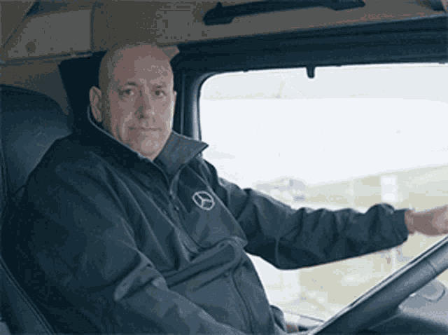 a man wearing a black jacket with a mercedes logo on it is driving a truck