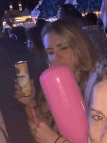 a woman is blowing up a pink balloon while holding a can of corona