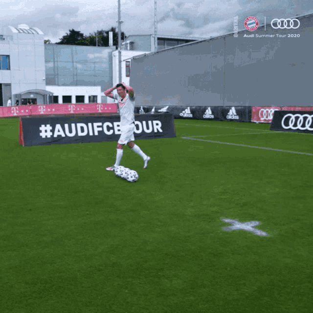 a man stands on a soccer field in front of a sign that says #au fcbtour