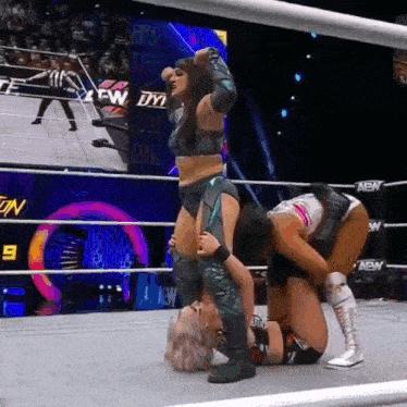 two women are wrestling in a wrestling ring with a referee standing in the background .