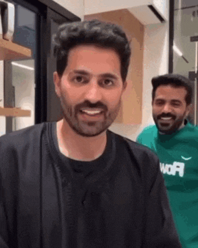 a man with a beard is smiling while standing next to another man in a green sweater .